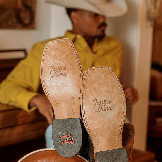 A Cowboy Leaning Against a Piano Bench Wearing the Sealy 13" Western Boots in Brown